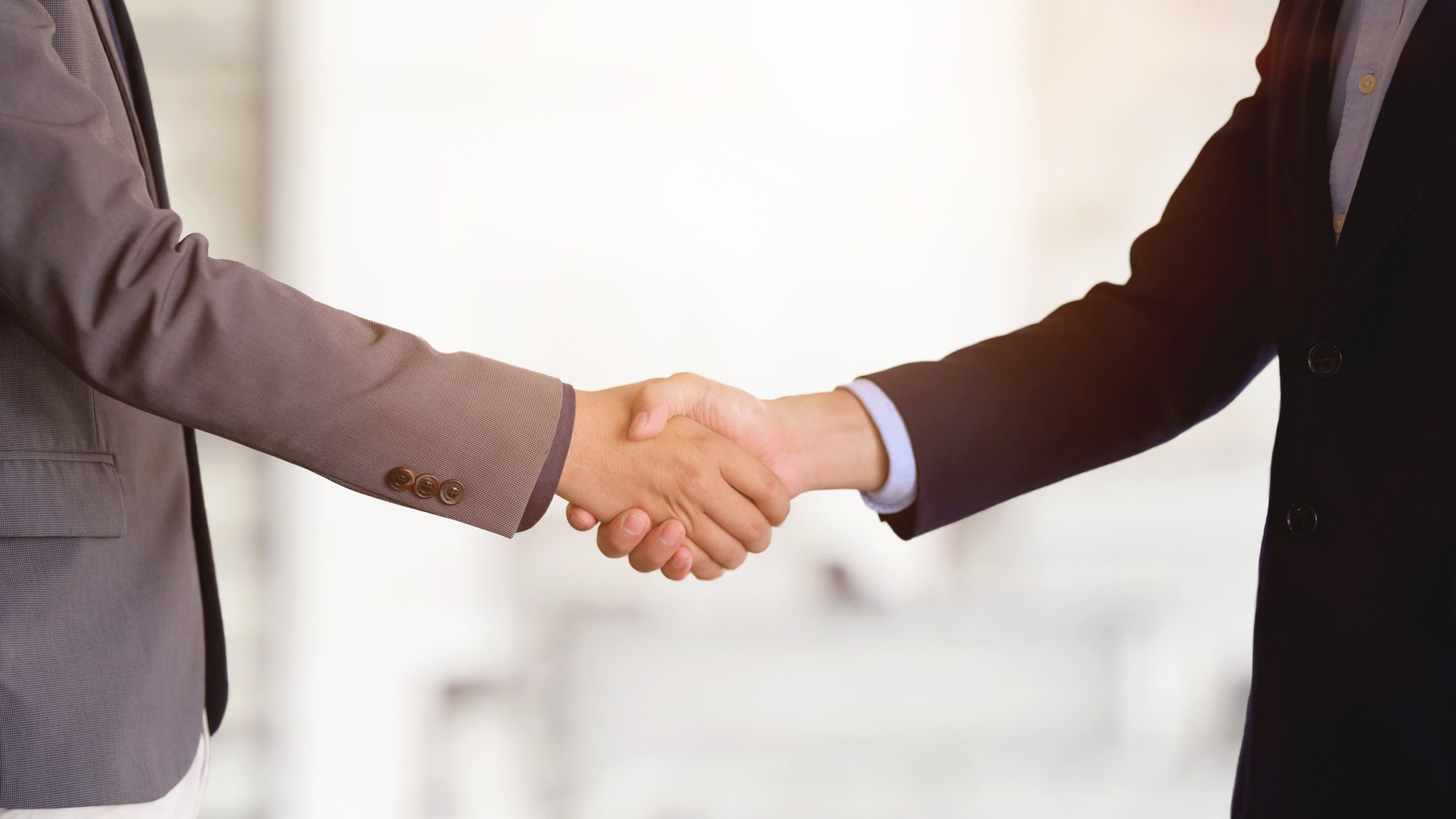 Crop businessmen shaking hands in light office